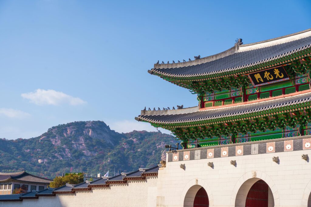 View of Gyeongbokgung Palace with traditional Korean architecture set against a mountain backdrop on a sunny day.